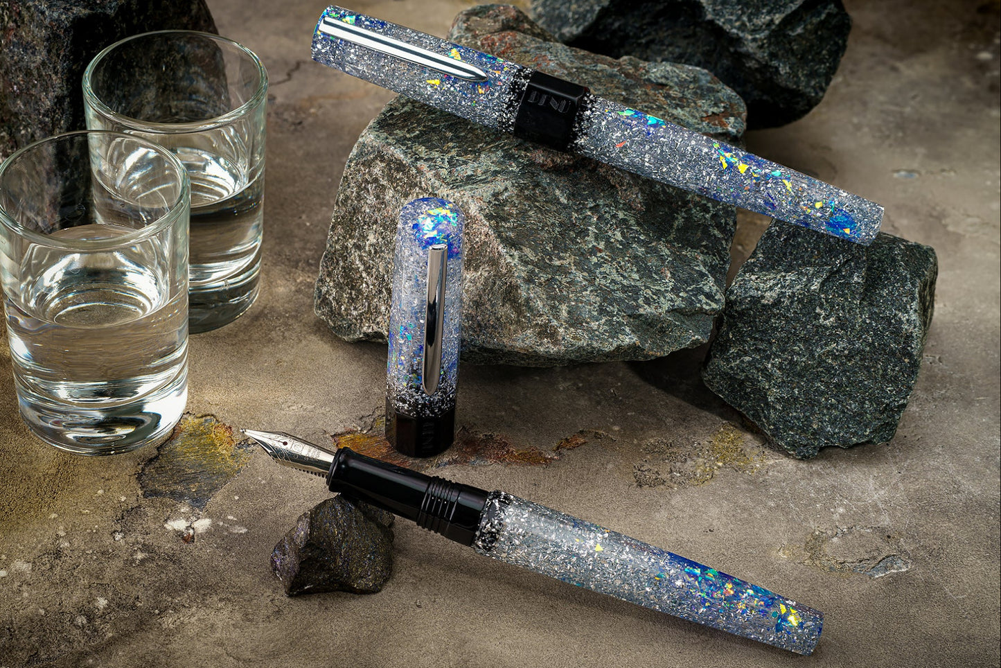 Fountain pen with glittery accents on a stone surface with glasses of water.