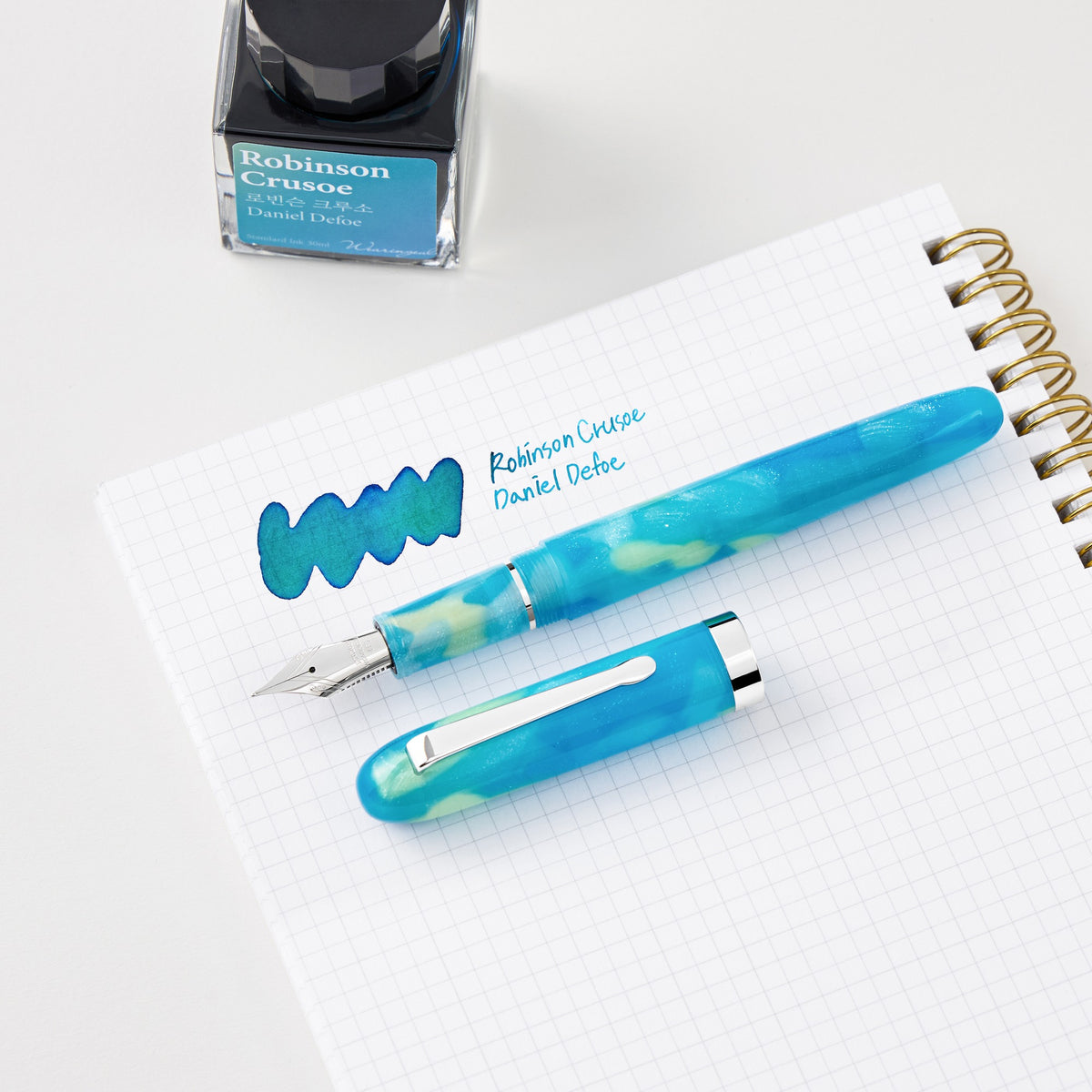 Wearingeul Robinson Crusoe fountain pen on a notebook beside matching ink, sold separately